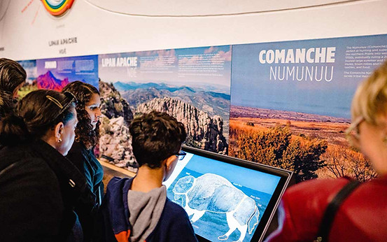 Children in a museum exhibit play an interactive game on a touchscreen, a bison is on the screen