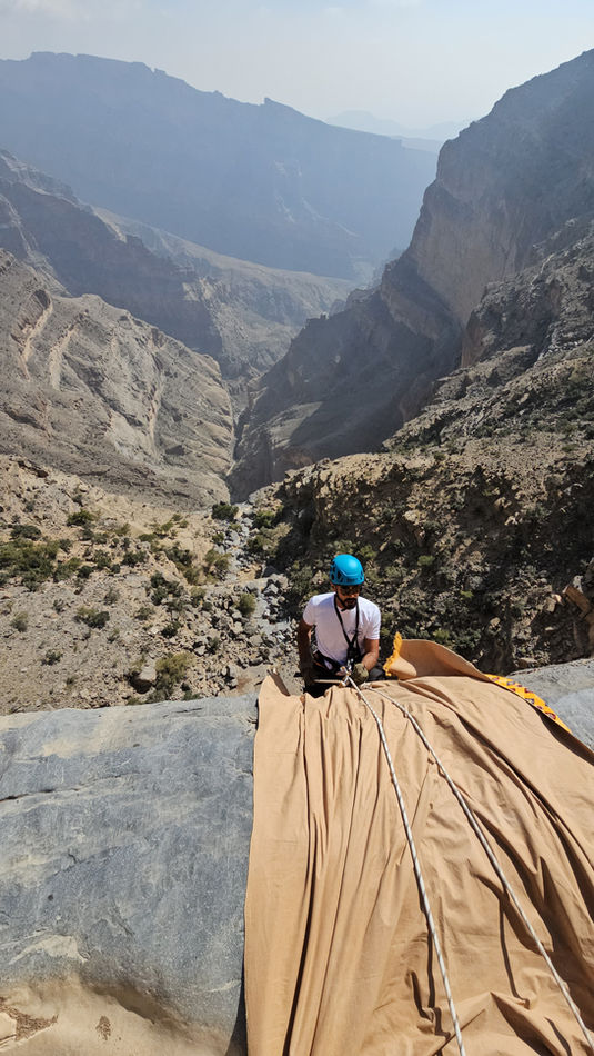 Participant standing on a wooden platform above the canyon during the Jabal Shams abseiling and via ferrata adventure in Oman