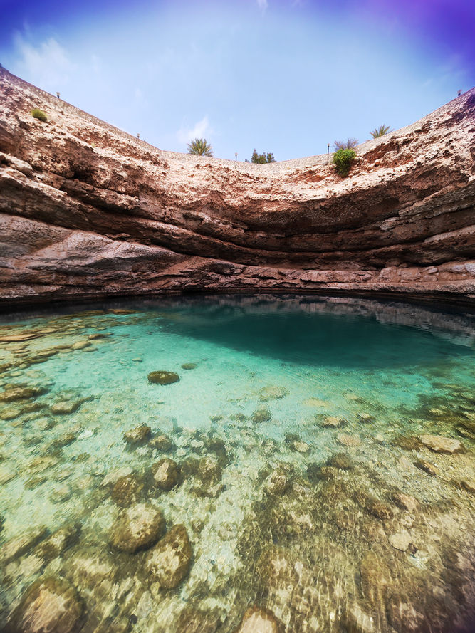 Clear emerald pool beneath layered rock walls in Wadi Shab on a guided day trip from Muscat