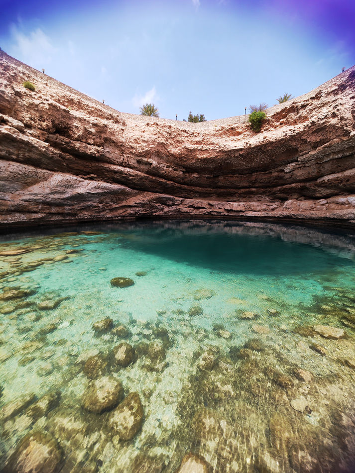 Clear emerald pool beneath layered rock walls in Wadi Shab on a guided day trip from Muscat