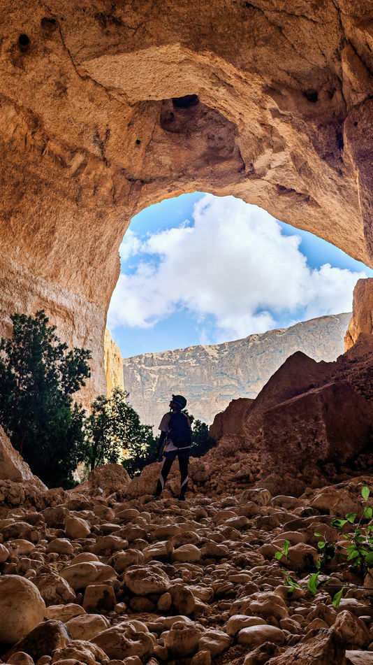 Cavers walking beneath the large entrance of Tahry Cave during a one-day caving adventure in Oman