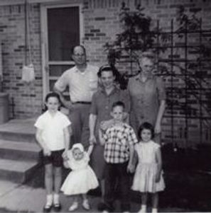 Black-and-white family portrait with adults and children outside a brick house.