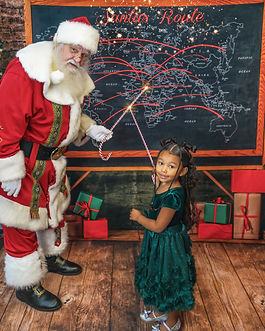 Santa and child stand in Santa's North Pole mailroom and look at the Christmas Eve flight path
