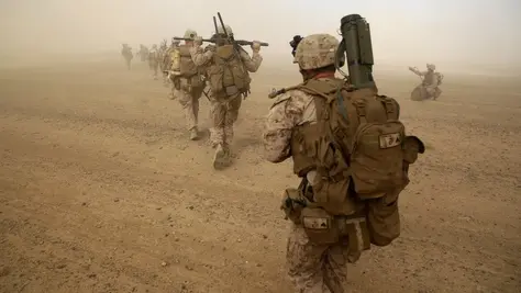 U.S. Marines advance through a dusty landscape, fully equipped for their forward deployment mission.