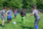 Five children, four boys and one girl, on a grass field playing with a soccer ball