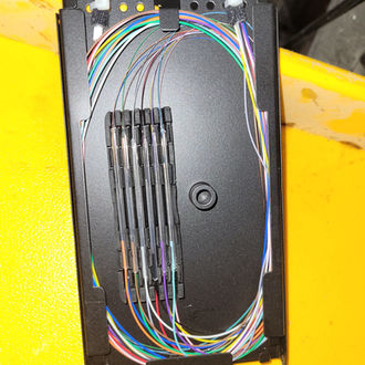 Fully populated fiber splice tray with neatly managed buffer tubes and fusion splices, representing expert fiber optic splicing and cable management.