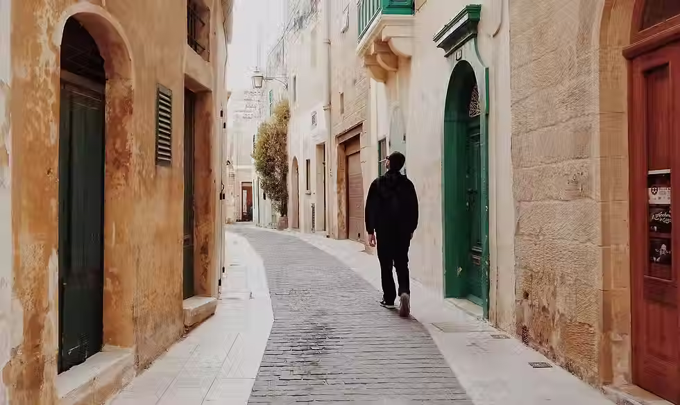 Traveler exploring a charming, narrow alley lined with stone buildings and green shutters, evoking the essence of cultural travel.