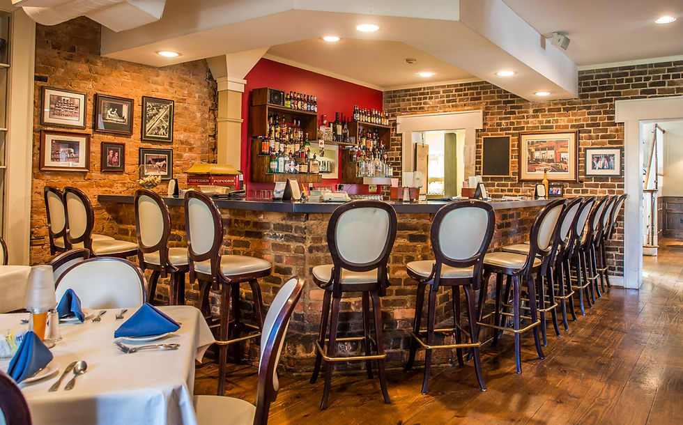 The bar and part of dining tables at Calhoun Corners Restaurant; tall bar stools with backs sit around the curving brick bar in front of brick walls, rows of bottles, and a terraced ceiling.