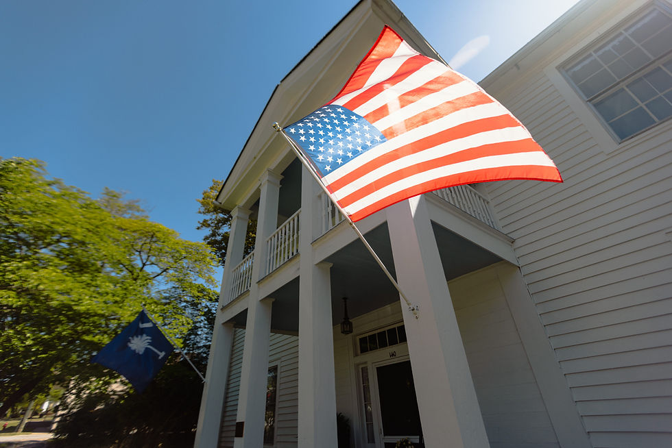 An American flag and South Carolina flag blow in the wind outside a white building in Pendleton