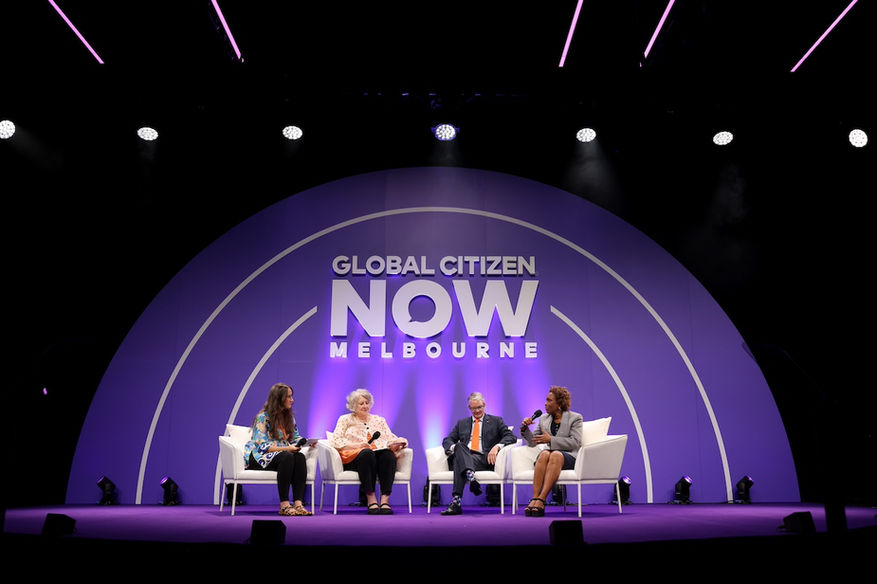 Four people sat on white chairs on a stage with a purple background