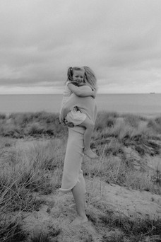 Mutte rund Tochter umarmen sich, im Hintergrund sind Ostsee und Dünen zu sehen. Familienfotografie Graal Müritz.