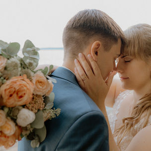 Hochzeitsfotograf Stralsund : Inniges Brautpaar am Wasser; sie lehnen die Stirn aneinander, im Vordergrund ein Brautstrauß mit apricotfarbenen Rosen