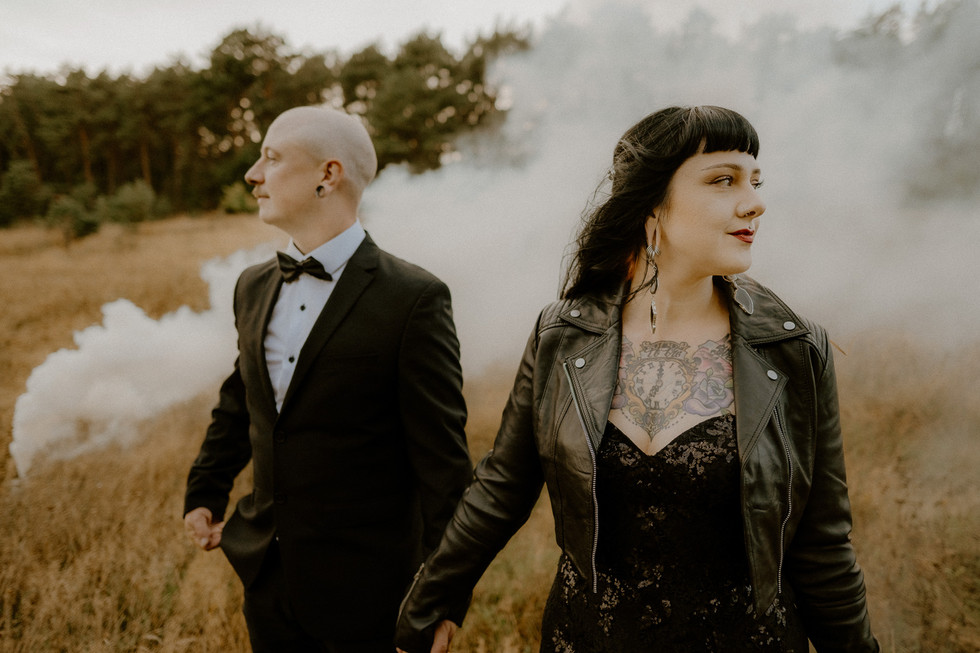 Tätowiertes Brautpaar steht bei einem Fotoshooting mit Rauchbomben auf einer Wiese. Unkonventionelle Hochzeitsfotografie Wolgast und Anklam.