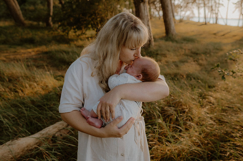 Mutter küsst liebevoll ihr Baby im Licht der untergehenden Sonne. Fotograf für Neugeborene in Karnin und Altenpleen.
