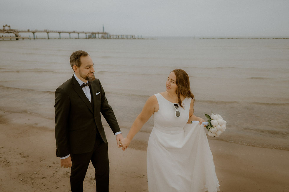 Klassische Hochzeitsportraits am Strand in Heiligendamm. Brautpaar spaziert an der Ostsee entlang - ist klassich gekleidet mit Sonnenbrille und Brautstrauß.