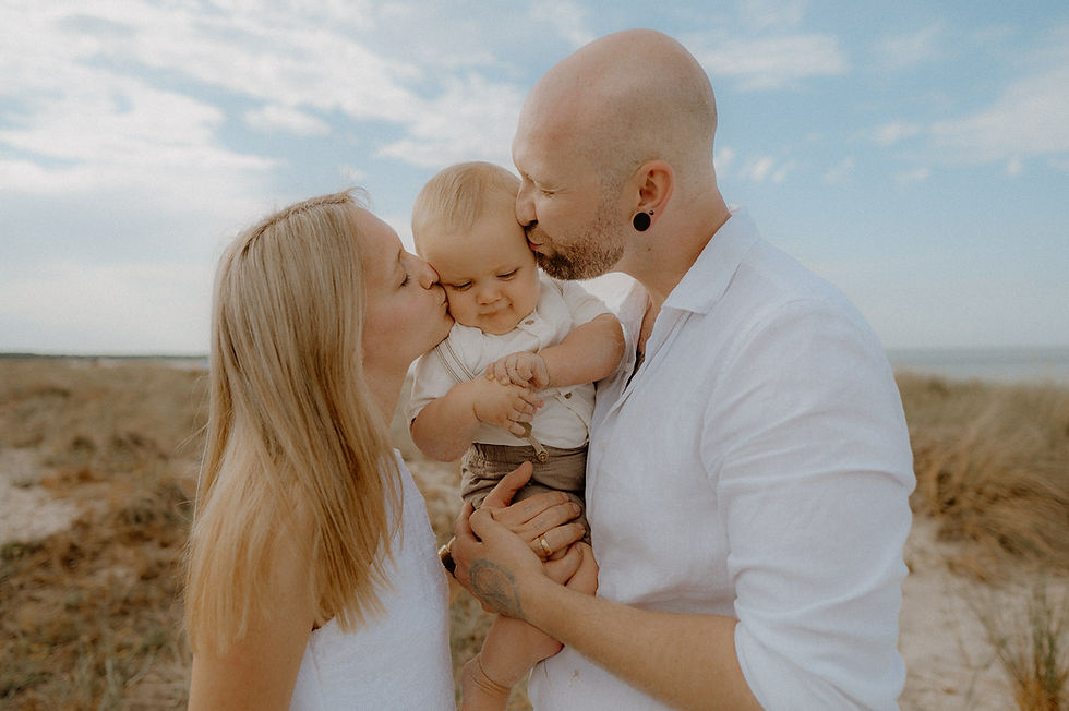 Liebevolles Familienfotos in Zingst an der Ostsee. Eltern halten ihr Baby im Arm und küssen es liebevoll!