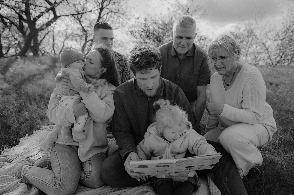 Generationenshooting Güstrow : Familie mit Großeltern sitzt im Gras auf einer Decke - lesen in einem Bilderbuch mit den Kindern.