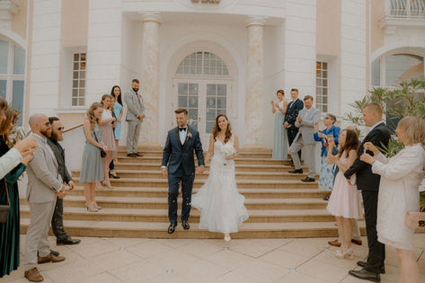 Hochwertige Hochzeitsplanung und Fotografie im Ostseebad Heringsdorf: Das Brautpaar schreitet die Treppe einer Villa hinab und lässt sich von den Gästen feiern.