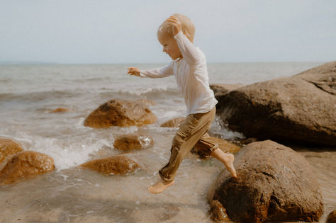 ein kleiner Junge springt von einem Stein an der Ostsee. Lebendige Familienbilder bei Rostock Wilhelmshöhe.