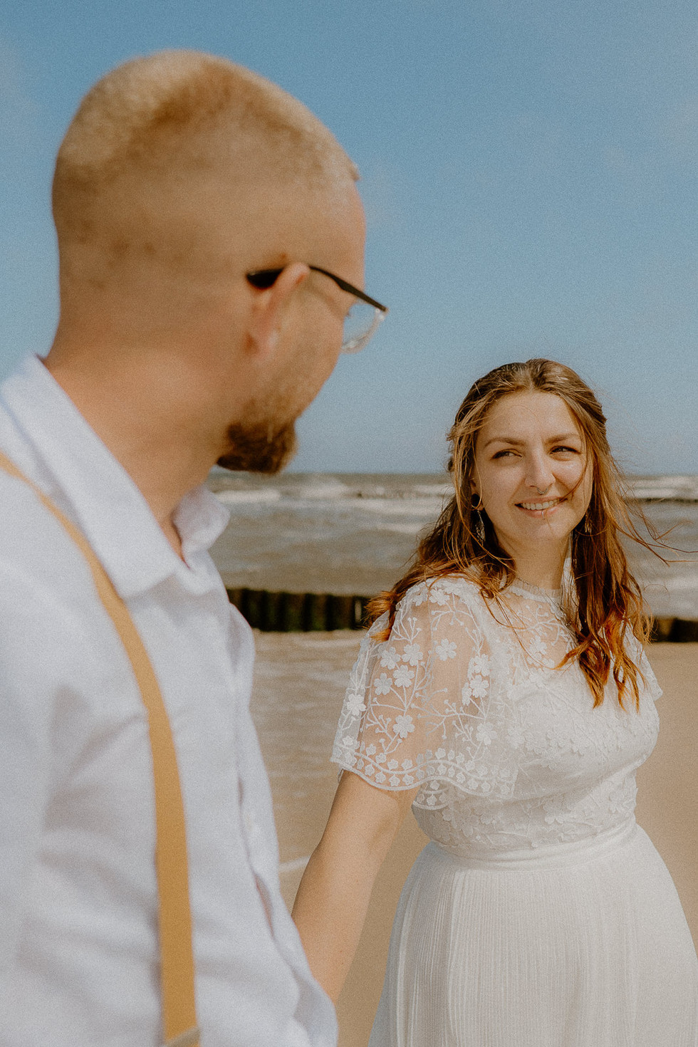 Braut lacht ihren Mann während eines Paarshootings in Zempin auf Usedom an. Verliebte Hochzeitsfotos in Zempin am Strand.