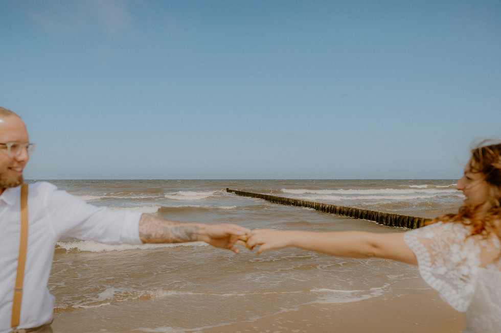 Paar hält sich fest an den Händen, im Hintergrund sieht man die rauschende Ostsee. Fotograf in Heringsdorf hält den Moment ganz natürlichfest.
