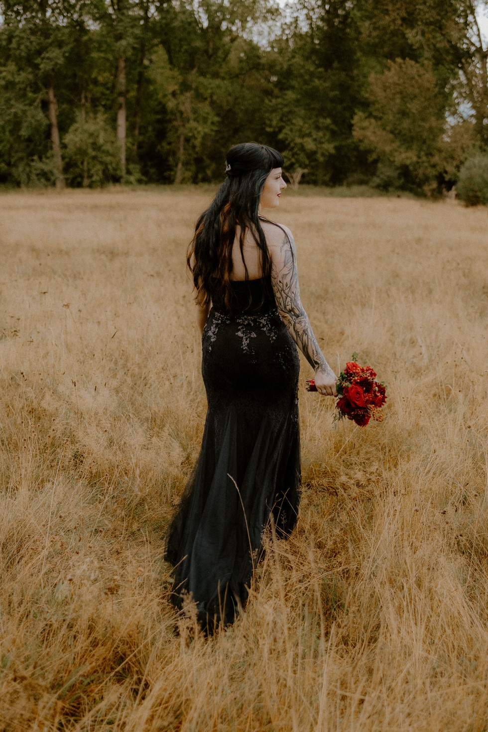 Wunderschöne schwarz gekleidete Braut auf einer Wiese. Fotograf begleitet Pärchen beim Fotoshooting.