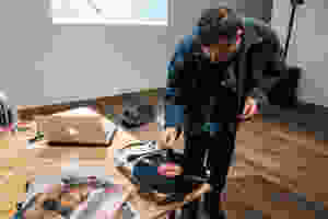 A man in jean jacket putting the needle on a record that sits on a table with some album covers.