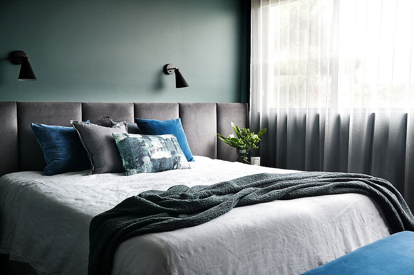 master bedroom with deep green walls, white sheer curtains, plush wall to wall bedhead, coordinated cushions
