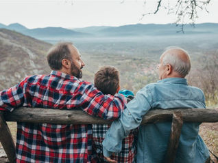 3 males - father, son and grandson sitting on a wooden bench with backs to camera looking out over a valley used on a blog about estate planning