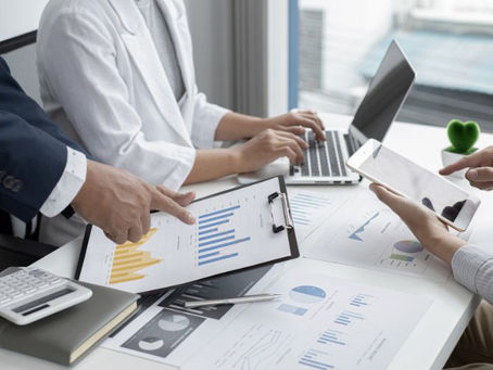 business meeting with 3 people whose faces aren't shown, one on a laptop, one on a tablet and one pointing at printed graphs used on a blog about the difference between a business loan and a business line of credit