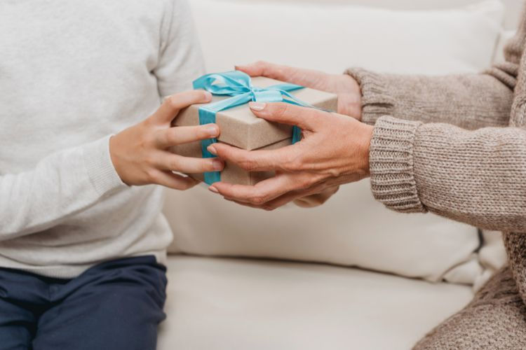 one set of hands handing over a gift box with ribbon to another