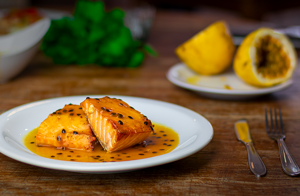Prato de dois pedaços suculentos de Salmão, com maracujás ao fundo.