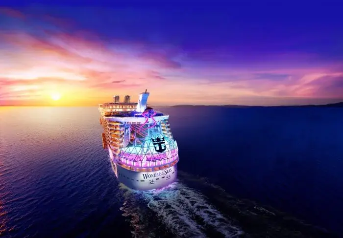 A colorful cruise ship sails at sunset. "Wonder of the Seas" is lit up, reflecting vibrant pink and blue hues on calm sea under a vivid sky.
