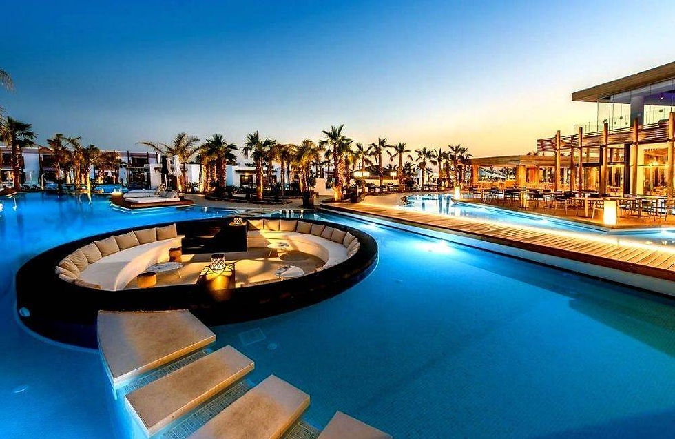 Luxurious resort pool at sunset with palm trees, circular couch area, glowing lanterns, and modern architecture. Relaxing and serene mood.