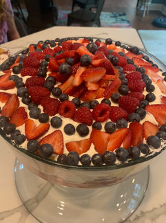 Summertime dessert with layers of angel food cake, berries and a custard in a large triffle glass dish. Red, white and blue dessert.