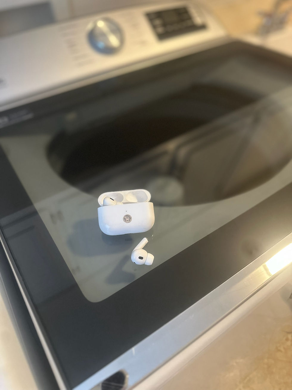 Earbuds and case on a washing machine lid. The setting is indoors with a focus on the sleek, modern appliance.