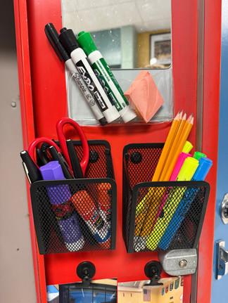 Red metal cabinet holds markers, pencils, and glue sticks in mesh holders. Scissors and sticky notes are visible. Office background.