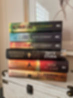Stack of five fantasy novels on a white chest: Kate Stewart and Rebecca Yarros titles, with colorful spines in a cozy room.