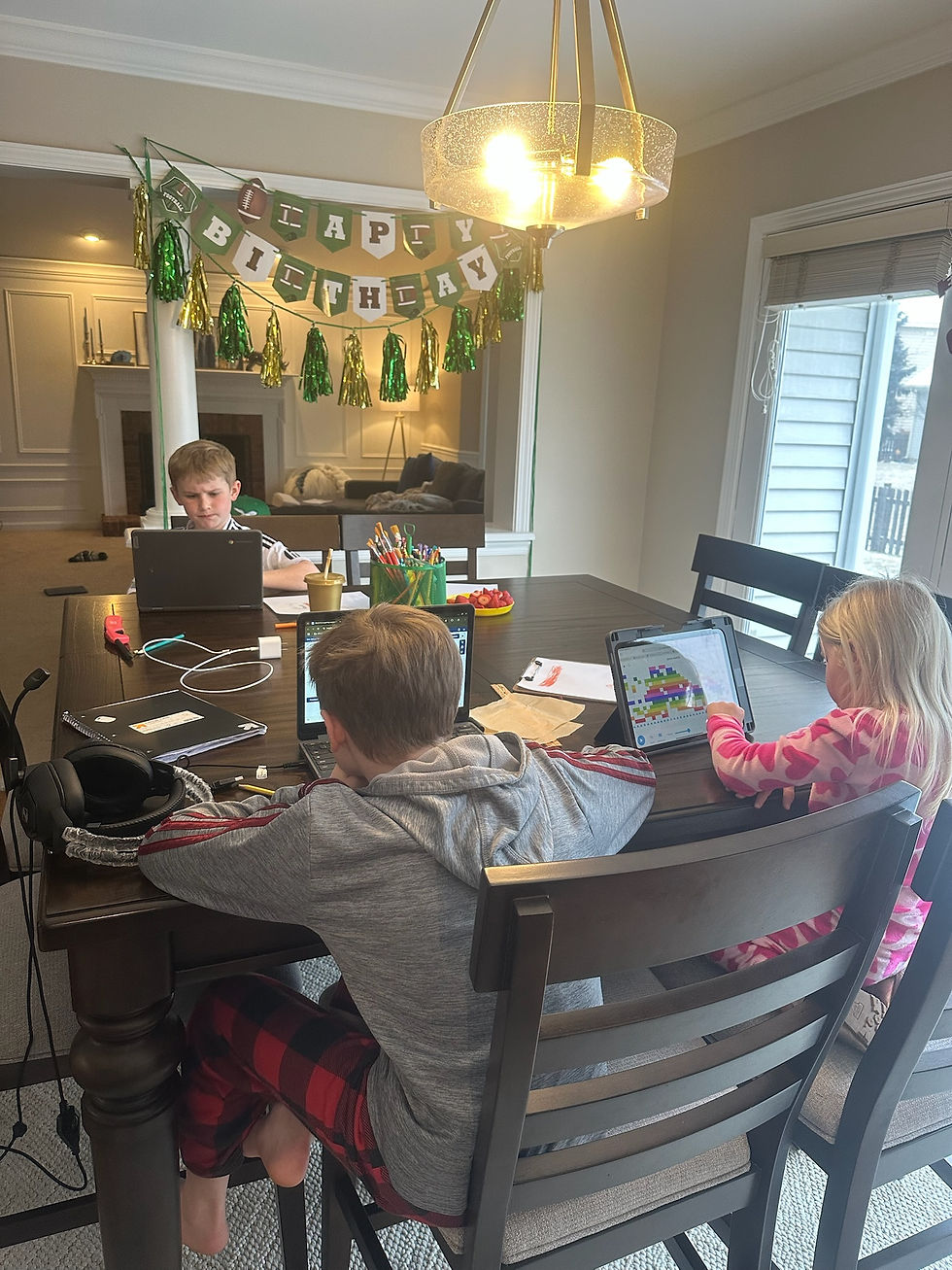Three children at a dining table work on laptops in a bright room, birthday banner in background. Cozy, focused atmosphere.