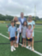 Family poses on a football field with a graduate holding roses and a diploma, all smiling under a cloudy sky.