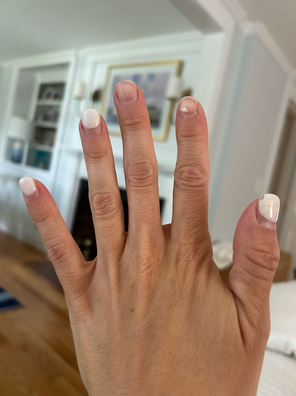 A hand with chipped white nail polish is shown against a background of a cozy living room with wooden flooring and a framed picture.