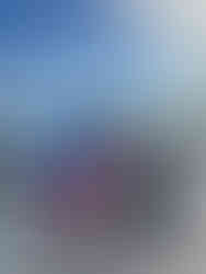 A family on a beach by cars, under a bright sky. They're barefoot, smiling, and one child is held. Vibrant clothes with visible logos.