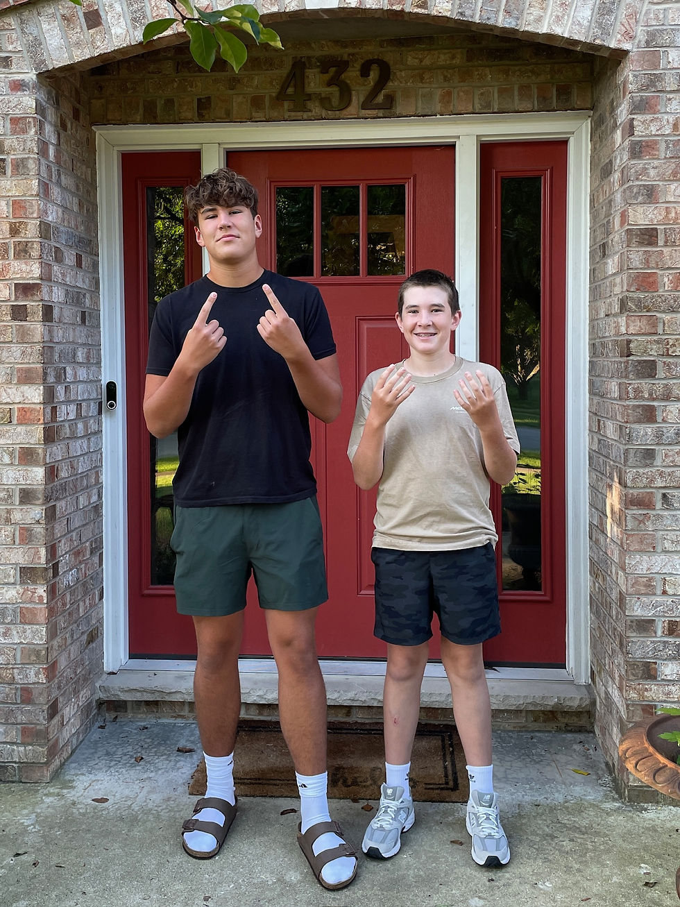 Two boys stand on a porch in front of a red door, holding up fingers in a playful gesture. House number 432 visible above the door.