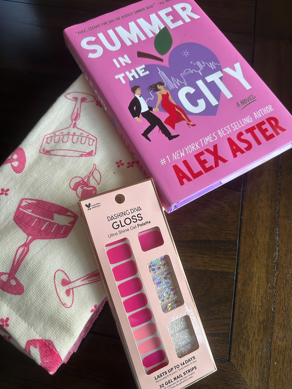 Pink book titled "Summer in the City" by Alex Aster, pink gel nail strips, cream fabric with red drink pattern on a wooden table.