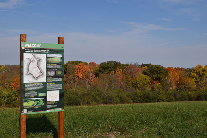 Informational welcome sign stands in a green field before an autumn forest.