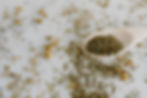 Dry herbs scattered on white surface with a wooden spoon holding more herbs. Varied textures and muted earthy tones create a natural look.