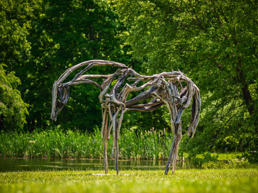 Driftwood horse sculpture in a green park near a pond.