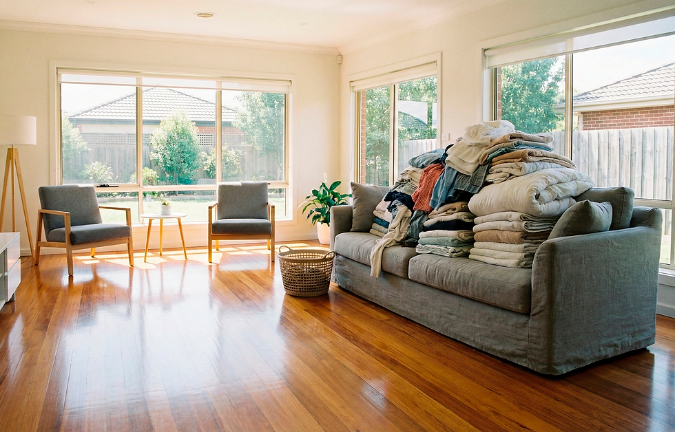 Spacious living room with gleaming hardwood floors and dust-free furniture, contrasting with a large pile of clean but unfolded laundry on the sofa, illustrating the need for housekeeping laundry add-ons in Maryland homes.