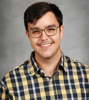 David St. Peter, Share Coordinator in a yellow and black plaid button down shirt with a gray background