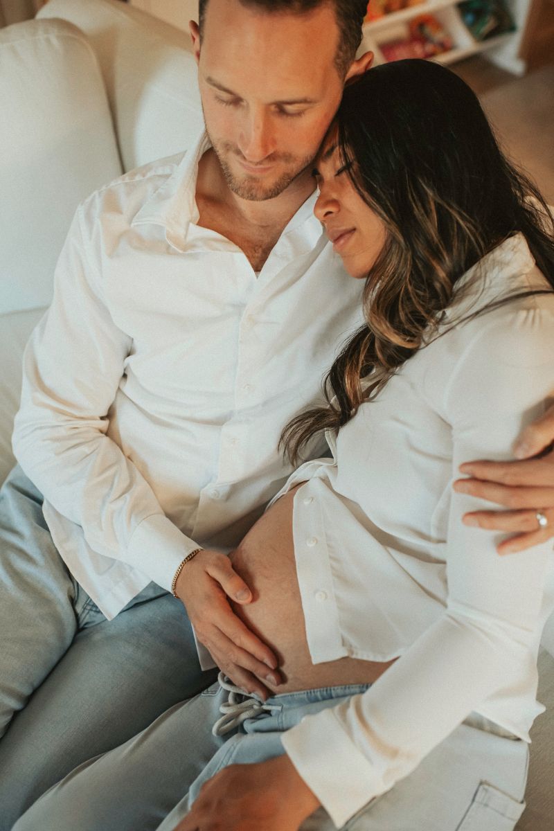 Mom and dad sitting on the couch and dad is rubbing moms belly